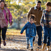 foto de un padre hispano y una madre blanca caminando afuera por un parque en la temporada de otoño con su hija y su hijo